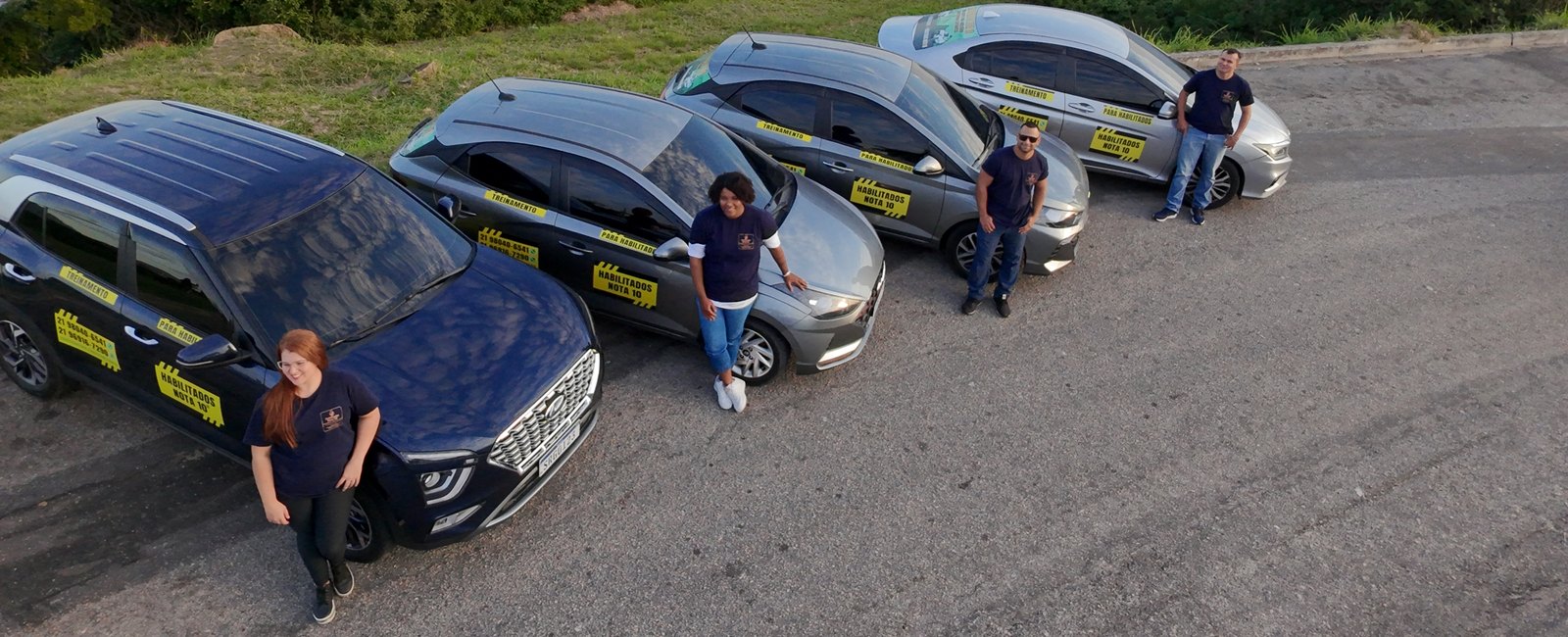 Os quatro instrutores da Habilitados Nota 10, cada um ao lado de um carro da frota, na orla de Niterói